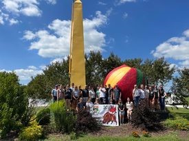 Outdoor group photo of the students on the 2023 Midwest Tour standing in front of a big peach