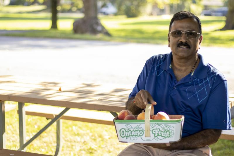Dr. Jay Subramanian sitting down with a basket of Ontario peaches