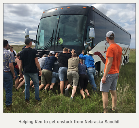 students pushing out the tour bus that is stuck in a field